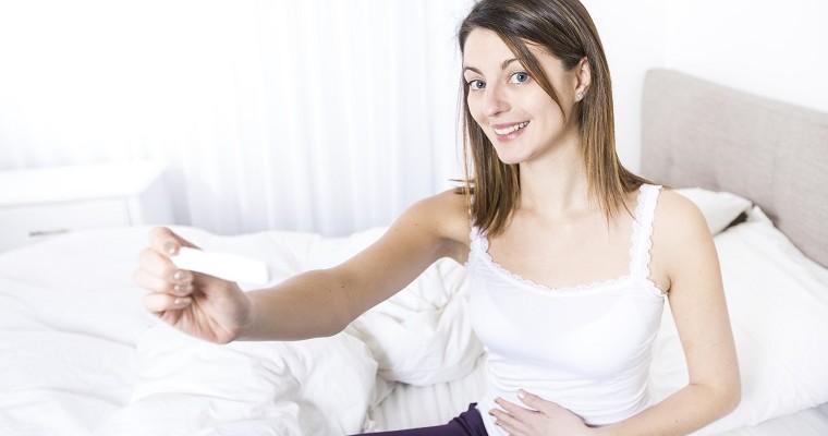Kobieta siedzi na łóżku i pokazuje test ciążowy