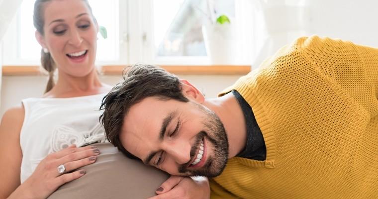 Mężczyzna przykłada ucho do brzucha kobiety w ciązy