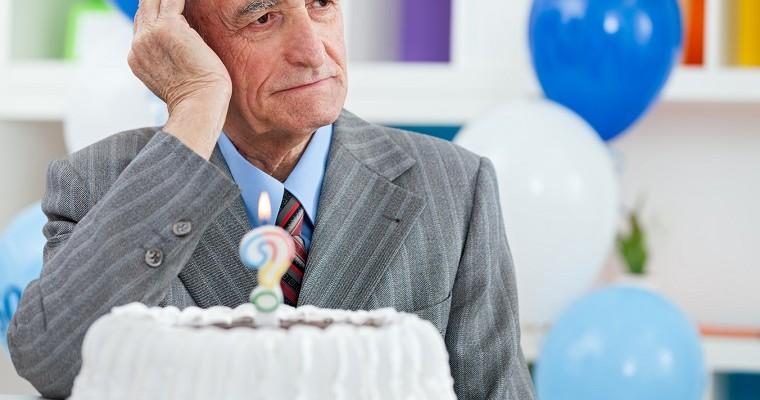 Starszy mężczyzna patrzy zamyślony. Na stole znajduje się tort urodzinowy ze świeczką w kształcie znaku zapytania
