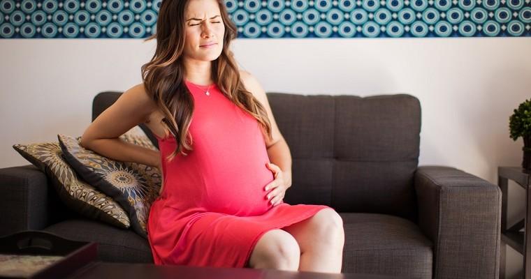 Kobieta w ciąży siedzi na kanapie i trzyma się za plecy z bólu