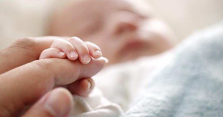 Noworodek trzyma w dłoni palec matki. 