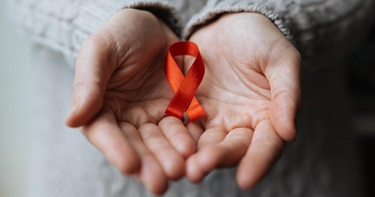 Kobieta trzyma w dłoniach czerwoną wstążkę - symbol walki z wirusem HIV