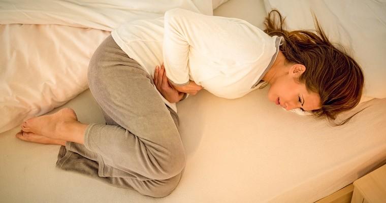 Kobieta podczas menstruacji z bólem brzucha leży zwinięta w kłębek na łóżku. 