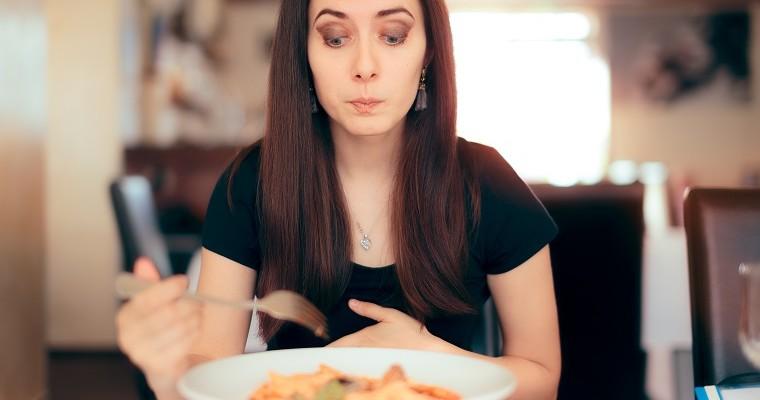Kobieta je posiłek i już przeczuwa problemy z układem pokarmowym. 