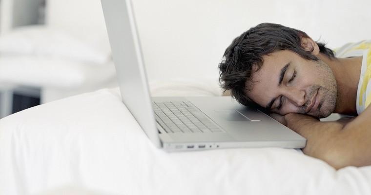 Mężczyzna śpiący przed laptopem. Jest szczęśliwy. 