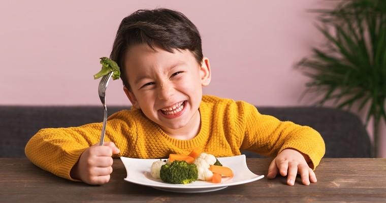 Dziecko je zdrowe warzywa z talerzyka. Uśmiecha się