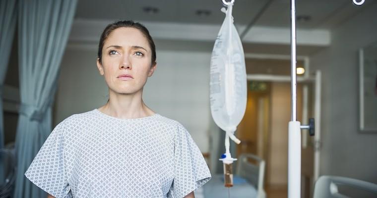 Smutna kobieta stoi w szpitalu. Jest podłączona do kroplówki.