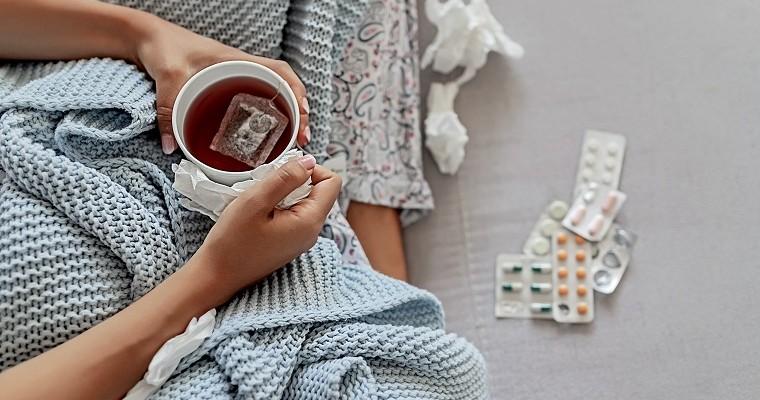 chora młoda kobieta leży w łóżku obok niej leżą leki 