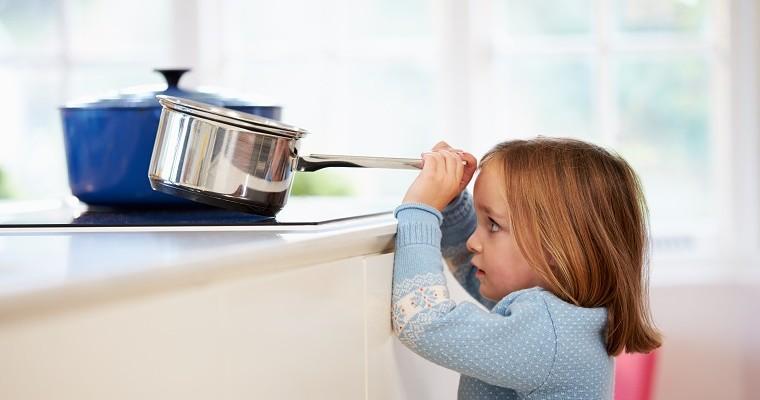 Mała dziewczynka w kuchni sięga po gorący rondelek