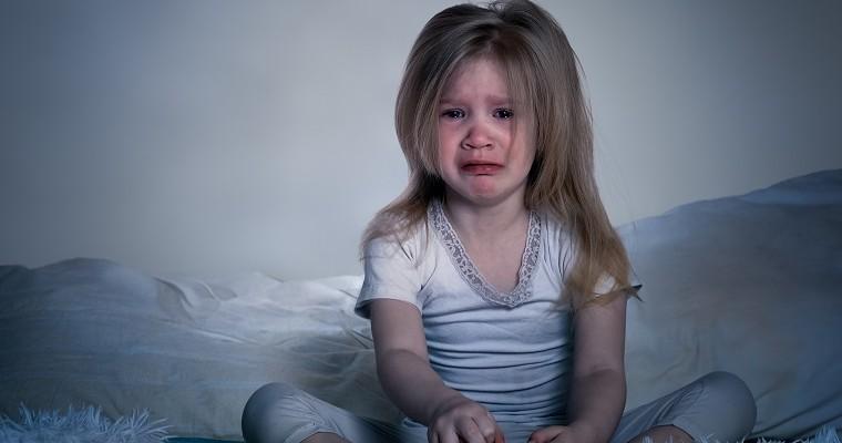 Mała dziewczynka siedzi na łóżku w piżamie i płacze.  