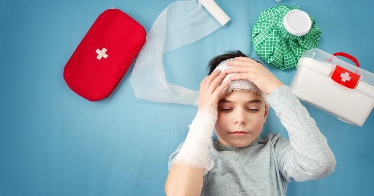 Dziecko z bandażami na głowie leżący w łóżku obok apteczka 