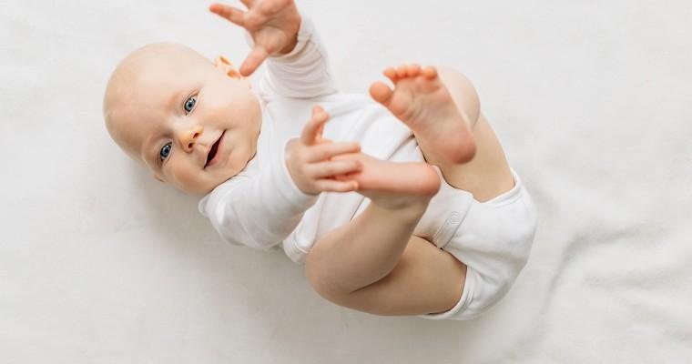 niemowlę leży na plecach, ręce i nogi podniesione do góry, patrząc na rodzica.