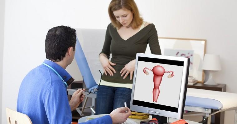 Kobieta wskazuje lekarzowi na swój brzuch, lekarz siedzi przed komputerem na którym wyświetla ryzunek jajników