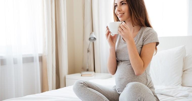 Kobieta w ciąży siedzi na łóżku i pije z filiżanki