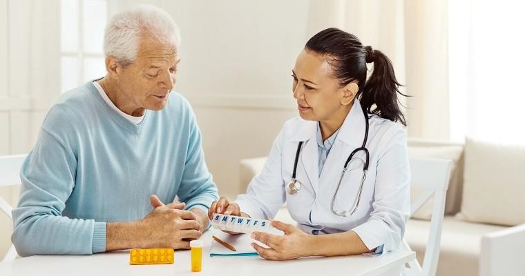 Starszy pan i lekarz siedzą przy stole i przeglądają leki